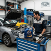 Un mecánico profesional con la equipación de Recambios Via Line prepara el mantenimiento de un Renault dCi en un taller. Sobre un carro de herramientas se muestra un kit de revisión compuesto por una garrafa de 5L de aceite Elf Evolution Full-Tech FE 5W-30 y un filtro de aceite original Renault, listo para ser instalado. Una flecha amarilla indica el proceso de mantenimiento en el motor.
